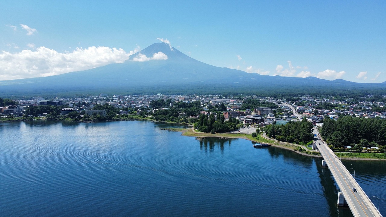 Panoramic view of Mount Fuji reflected in Lake Kawaguchi at sunrise, with cherry blossoms framing the shore