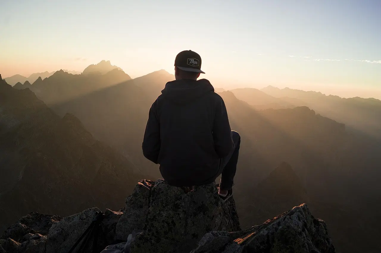 A lone hiker silhouetted against a golden alpine meadow with snow-draped peaks in the distance