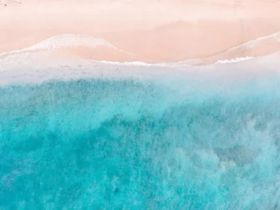 Aerial view of a quiet coastal cove with turquoise water, white sand, and lush green cliffs at sunrise