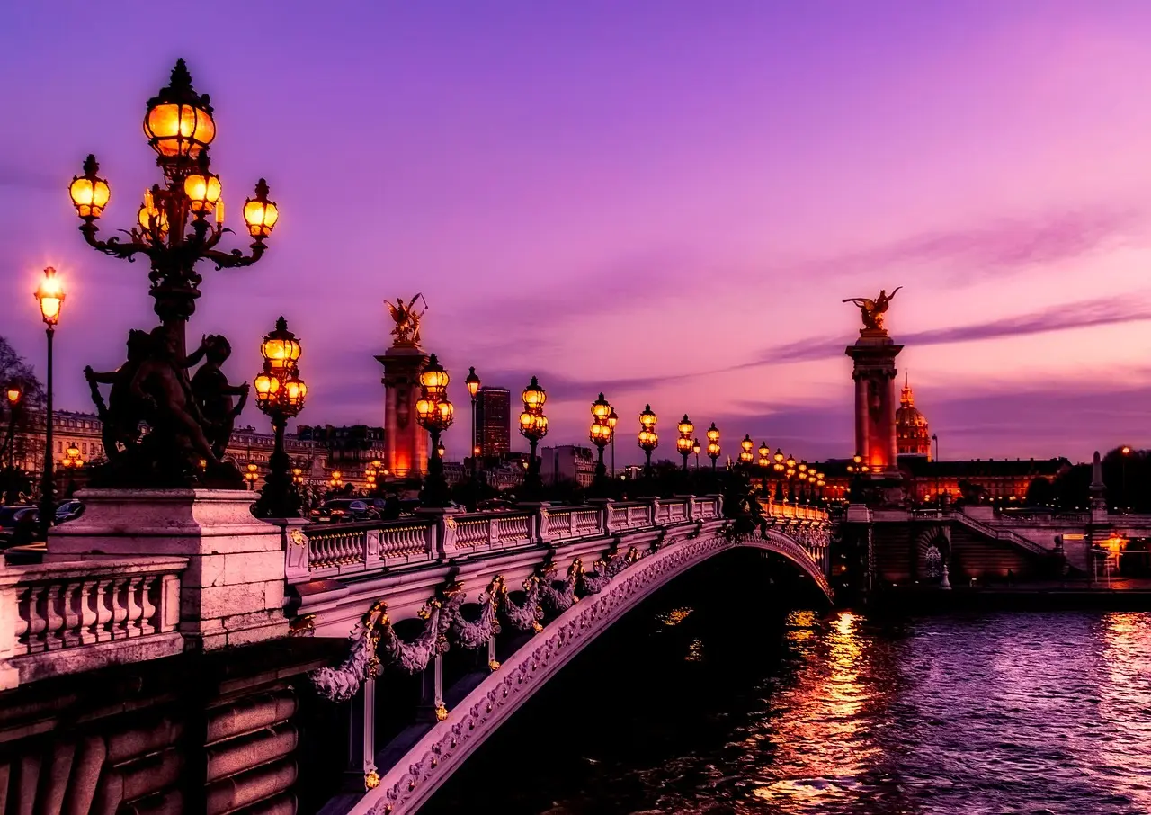 The Eiffel Tower mirrored in calm waters of the Seine — a dreamy, high-contrast composition that defines why Paris remains a top-tier travel destination for landmark photography Eiffel Tower reflected in the Seine River at sunset, with classic French street lamps along the quay